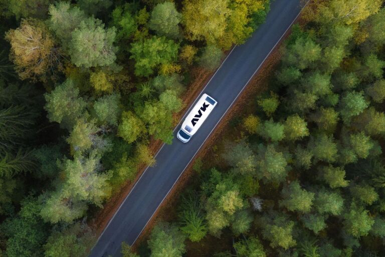 Aerial view of an AVK branded vehicle, driving on a road through a forest